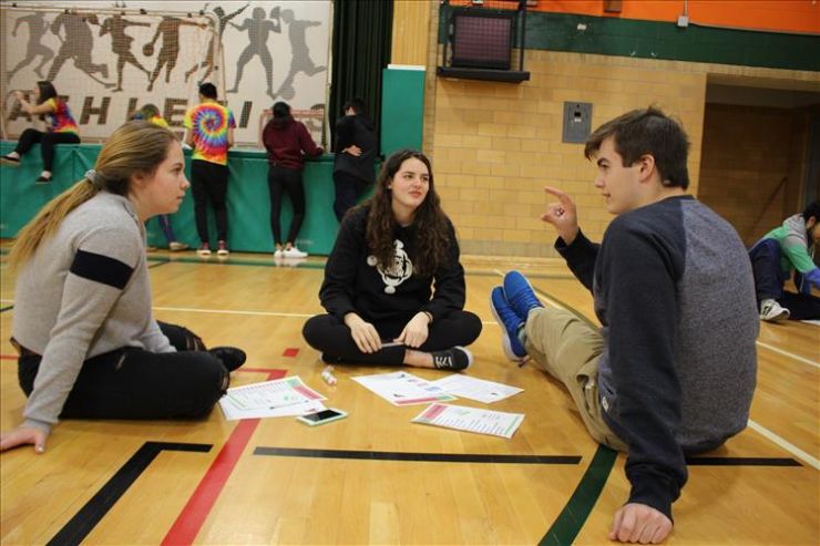 Three students seated in a gym make plans