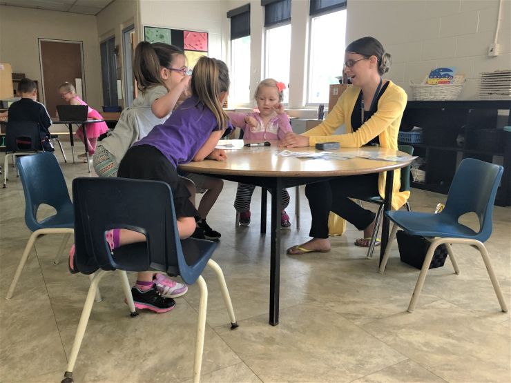 A teacher sits at a table with Kindergarten students