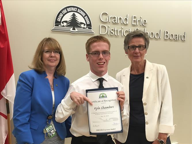 A young man smiles while holding a certificate with two staff members posing with him