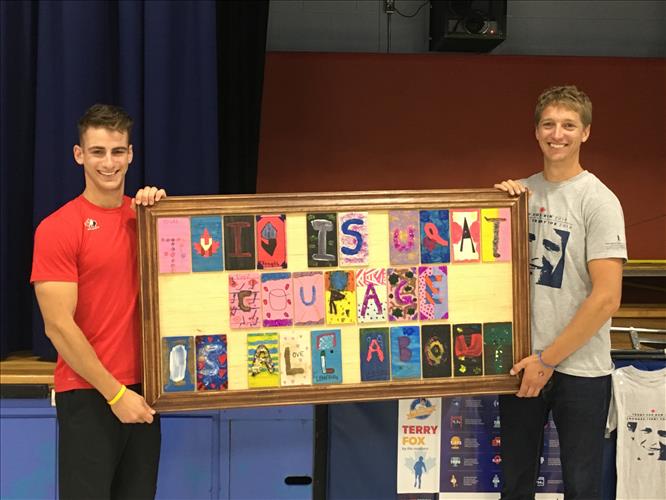 A teacher and an athlete hold up a poster with inspiring message