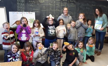 A group of young students smiles while holding healthy snacks
