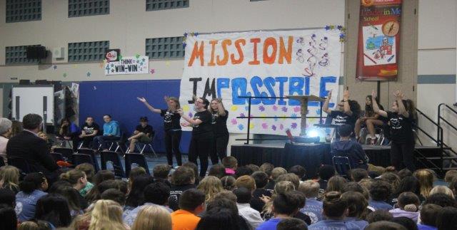 A pep rally takes place in a gymnasium with the words Mission Impossible on a large poster