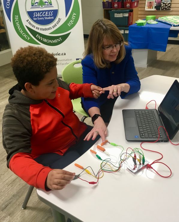 A woman is instructed by a young student using Makey-Makey technology 