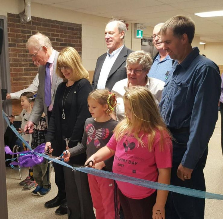 A group of students and staff cuts a ribbon in a school hallway