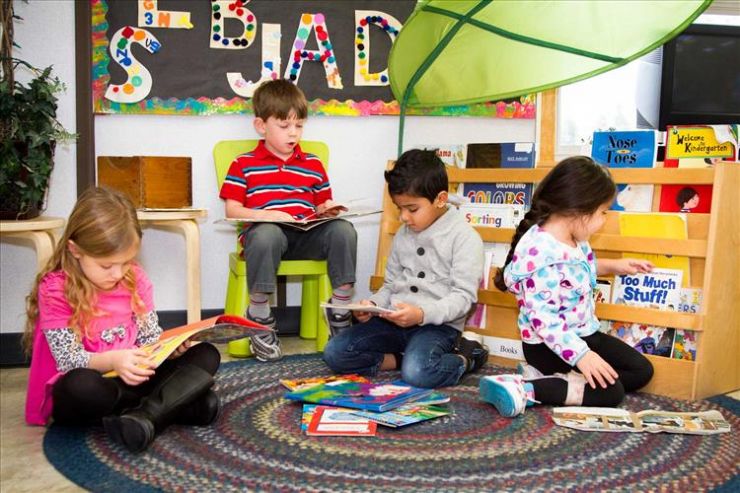 A group of four Kindergarten students sits on a mat playing with toys and books