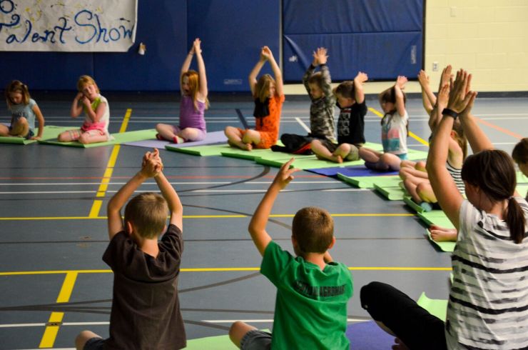 A group of students sit on yoga mats with their arms in the air