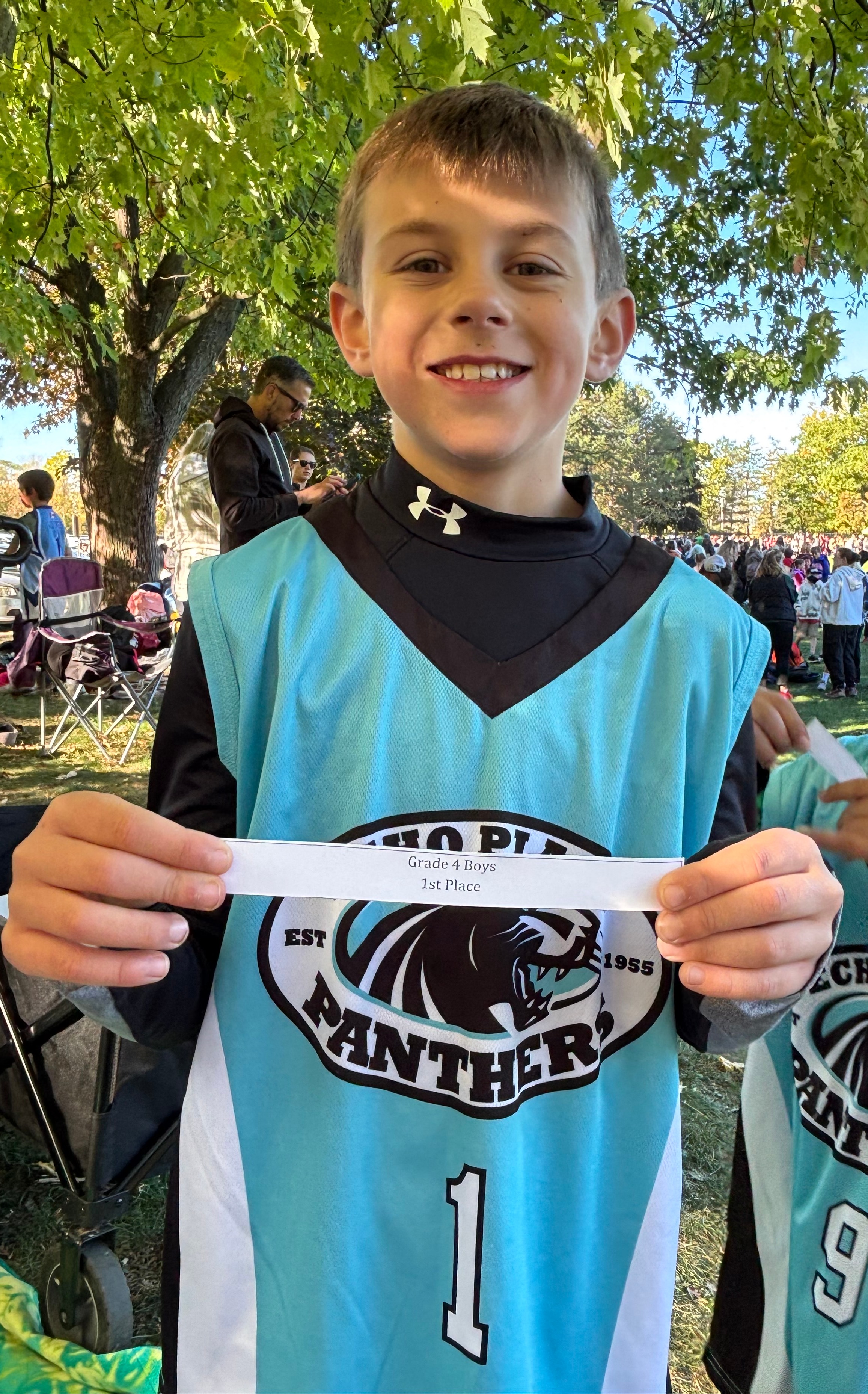 Grade 4 student wearing a school jersey is holding up a paper that says first place.